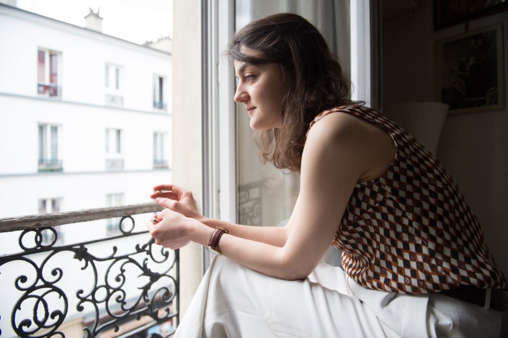 ©Gaël Dupret, France, Paris le 30-05-2017 : Portrait de Julie Pouillon Photo : Julie Pouillon restauratrice d'oeuvres d'art et fondatrice de l'Atelier Julie Pouillon. Son portrait a été réalisé dans son appartement et atelier parisien. Julie Pouillon pose devant sa fenetre. Elle fume, assise sur sa valise et regarde la rue.